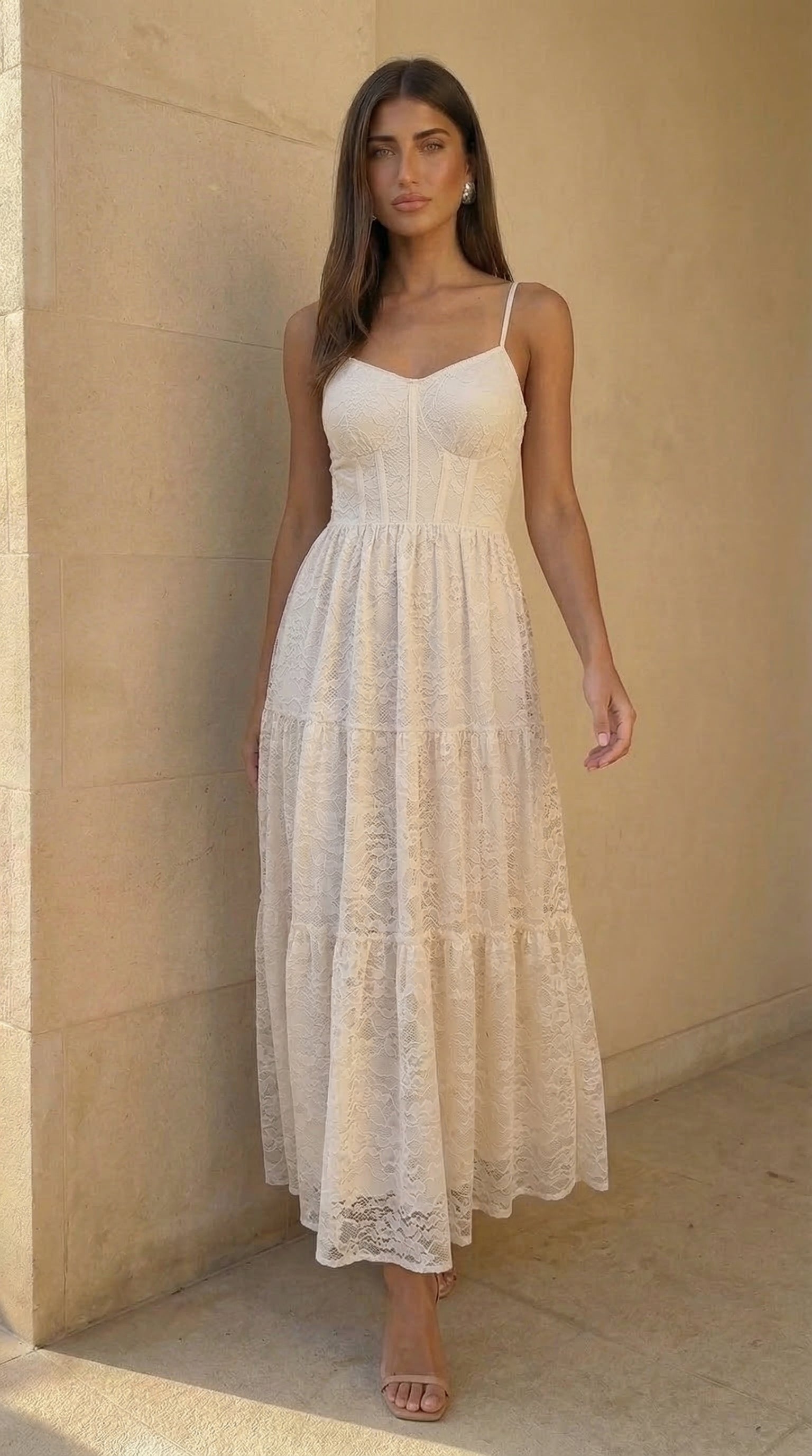 Woman wearing a white lace dress standing against a beige wall.